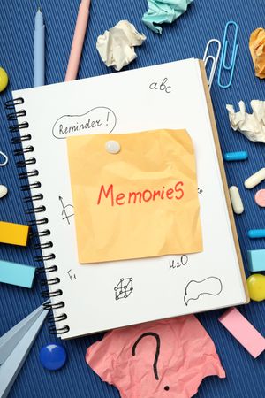 “Memories” post it note on book with pills, paper clips and pens on blue background, vertical
