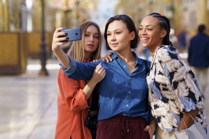 Three women taking selfie with phone in city