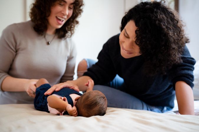 Two woman smiling down at baby on bed