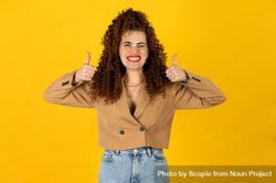Excited woman raising two thumbs up against yellow background 5pK680