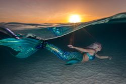 Blond fairytale female mermaid swimming along sea bottom