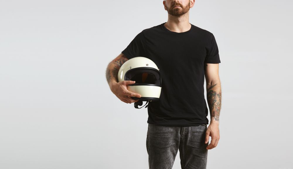 Tattooed man in dark t-shirt holding motorcycle helmet on light background