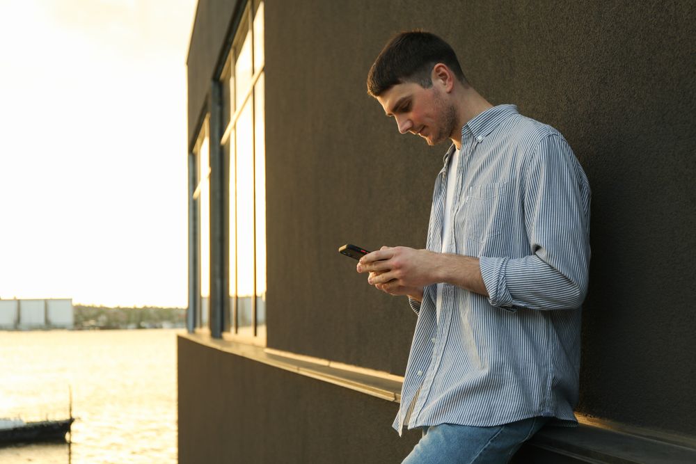 Young man uses a phone outdoor. Writing a message