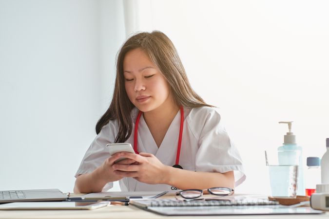 Focused Asian doctor browsing smartphone in hospital
