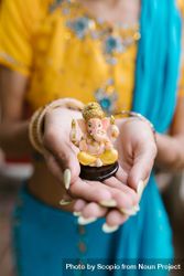 Cropped image of Indian woman wearing sari holding Ganesha figurine bxKGr4