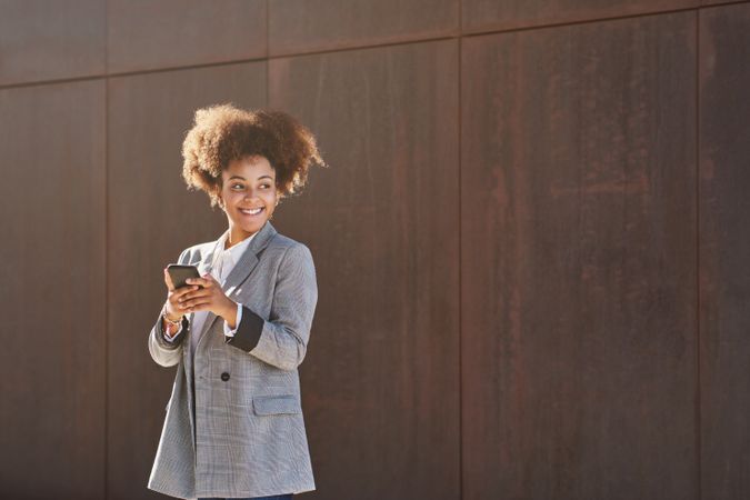 Glad Black woman using cellphone against gray wall