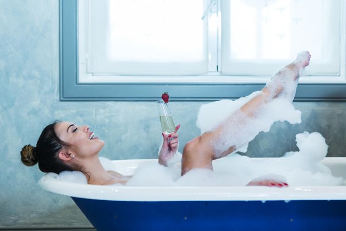 Cheerful woman with champagne laying in bathtub