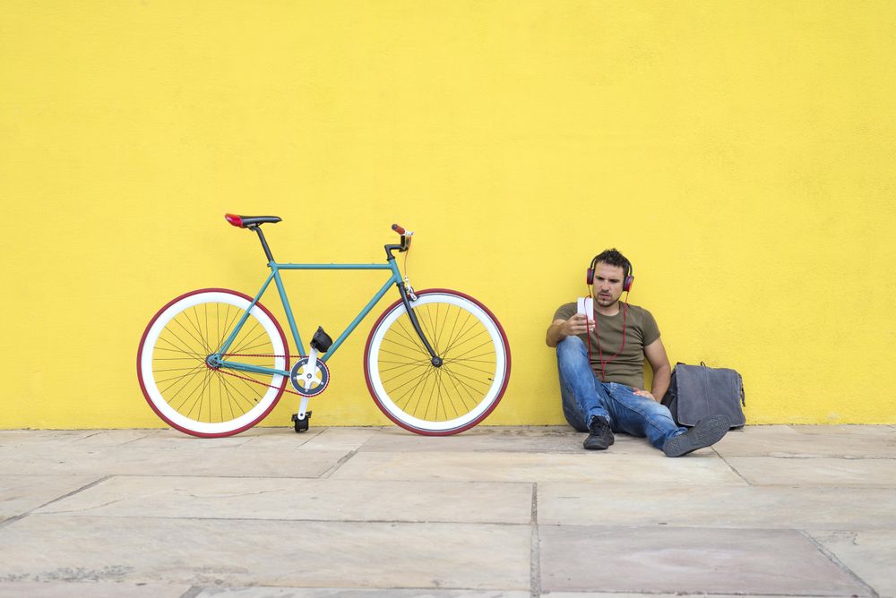 Man sitting in front of yellow wall with bike listening to music