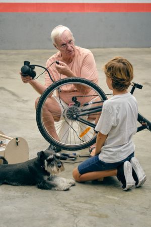 Grandfather pumping up bicycle wheel with grandson near dog