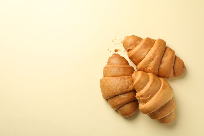 Three baked croissants on beige background, top view with copy space