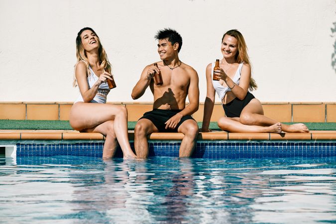 two young women and an asiatic man drinking beer by the pool