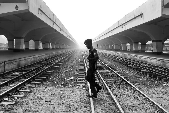 Side view of an army man standing on train rail in Dhaka, Bangladesh in grayscale