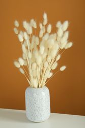 Vase of dried bunny tail bouquet centered on table in brown room, vertical composition