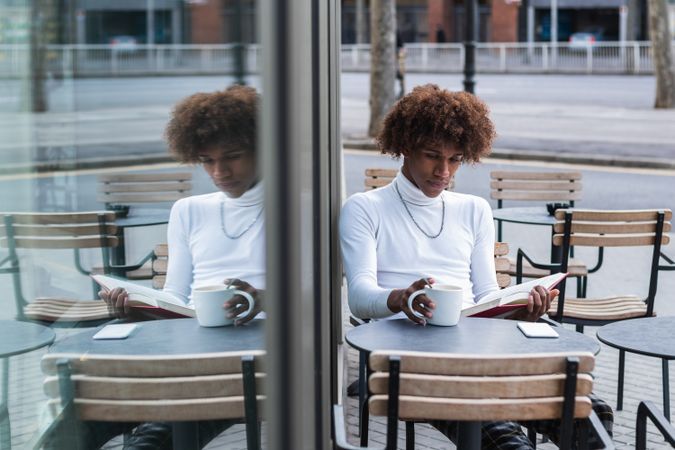 Relaxed young Black man reading book in street cafe