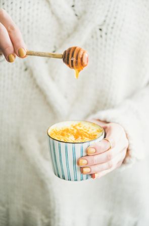 Female drizzling honey on top of warm turmeric latte