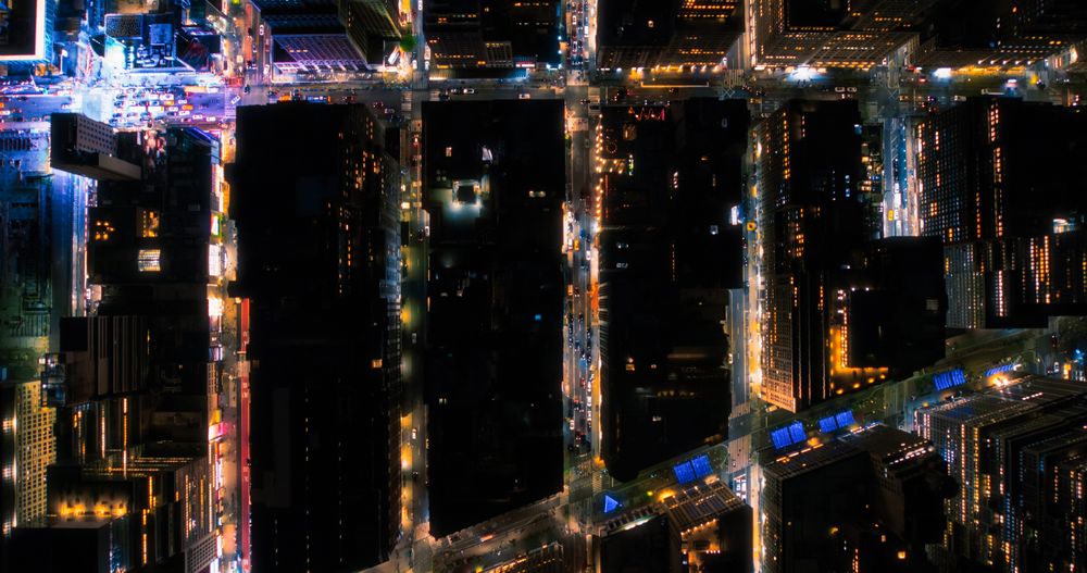 Top Down Aerial View of New York City Streets at Night with Visible Grid System, Business and Residential Building Roofs. Busy Center with Traffic, Cars, Yellow Taxis, Commercial Vehicles, Pedestrians