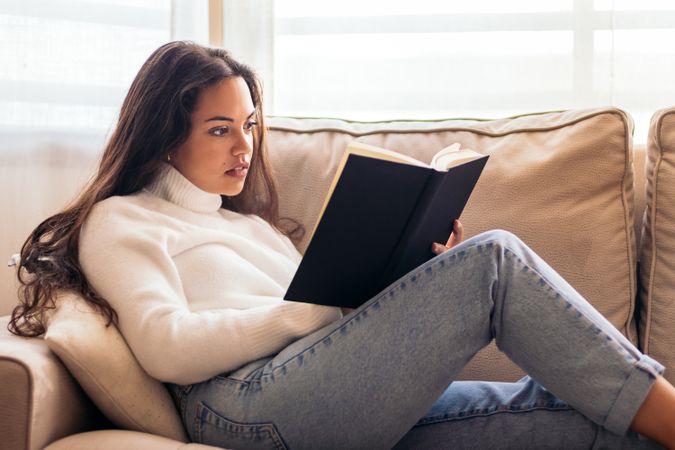 Relaxing at Home: Young Woman Reading a Book on the Sofa