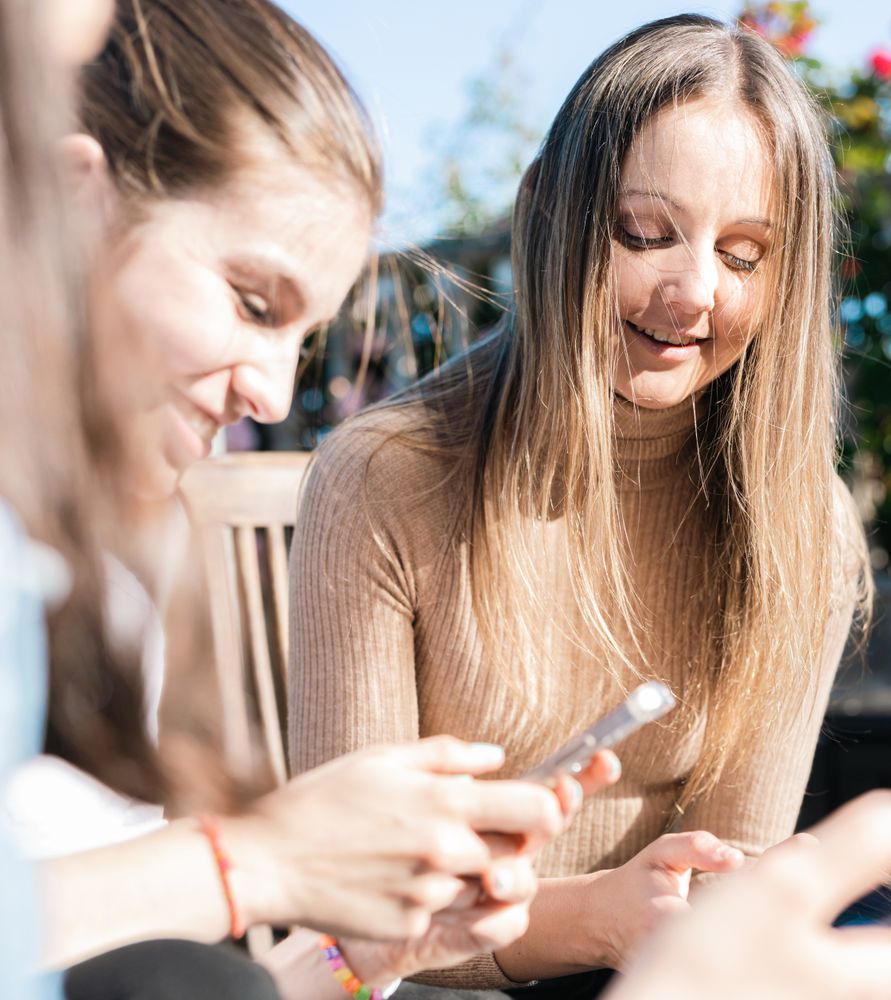 Young women taking a break from studying showing messages on phones while talking and laughing.