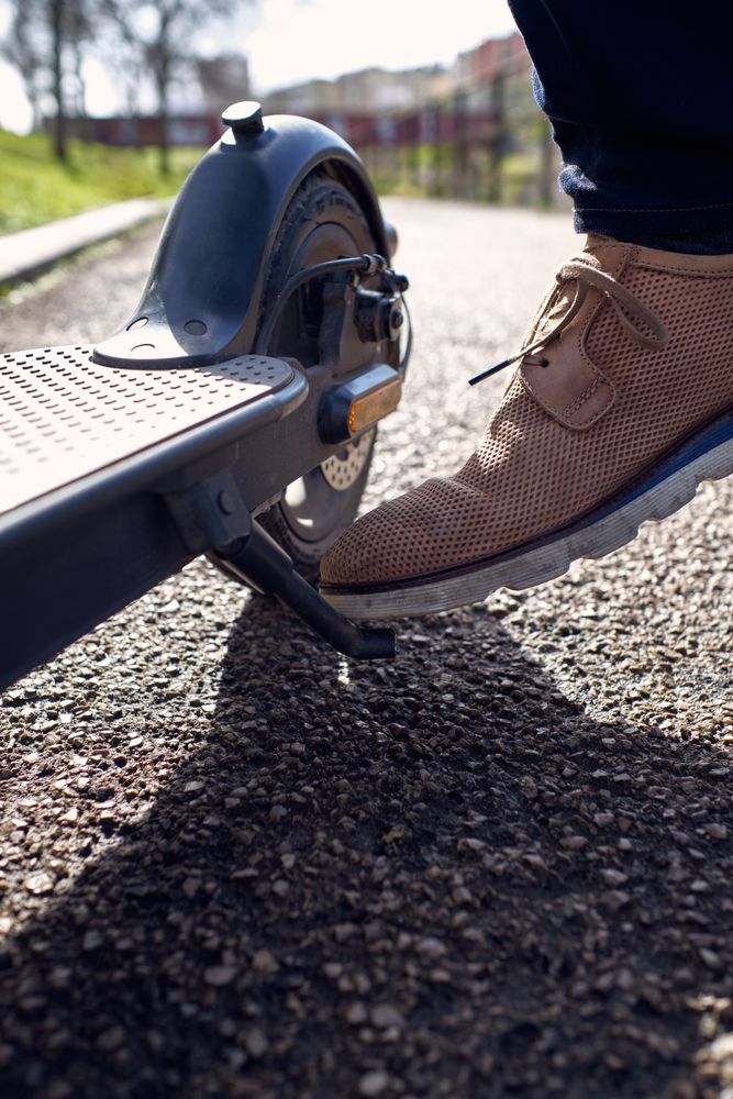 Crop man in stylish shoes parking electric scooter in city