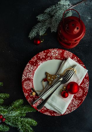 Top view of holiday table setting on red plates with lantern and pine needles