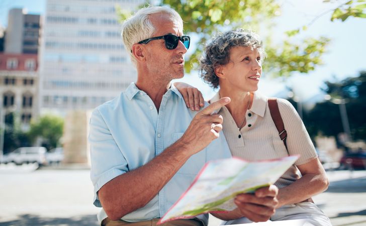 Older couple sitting outdoors in the city using map for finding directions