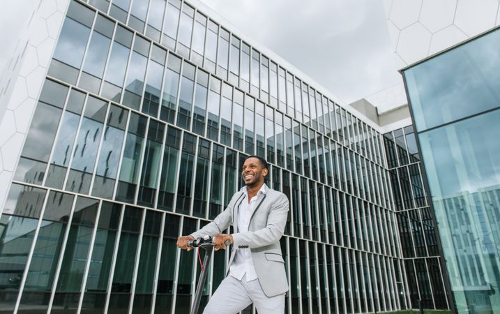 Black man in suit on electric scooter in business center