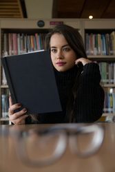 Woman sitting along bookshelves and holding open book