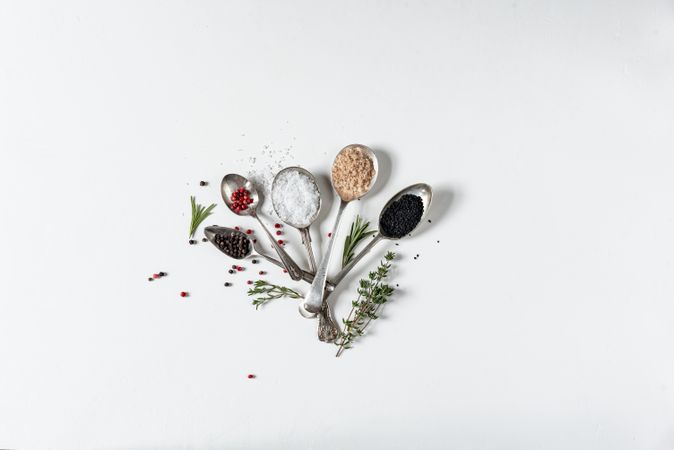 Spoons of salts, spices and herbs on light background
