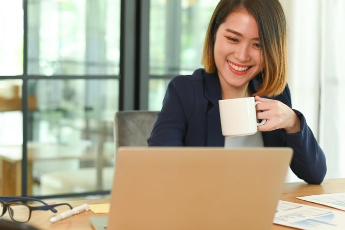 Smiling business woman drinking coffee during online meeting