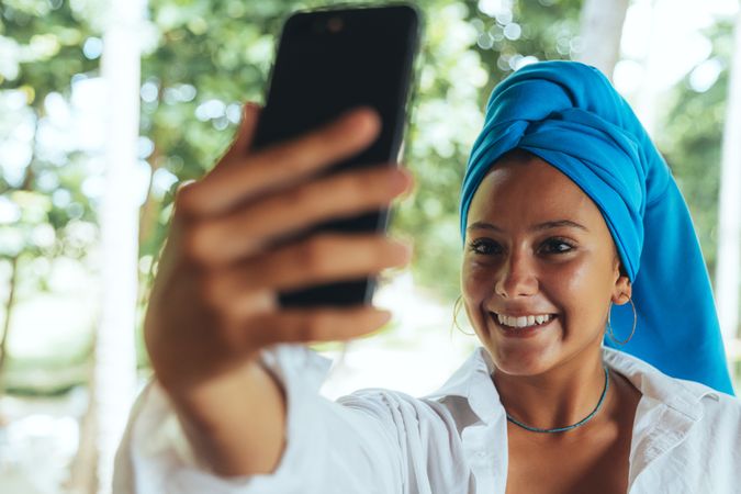 Positive woman with turban on head taking selfie on sunny street