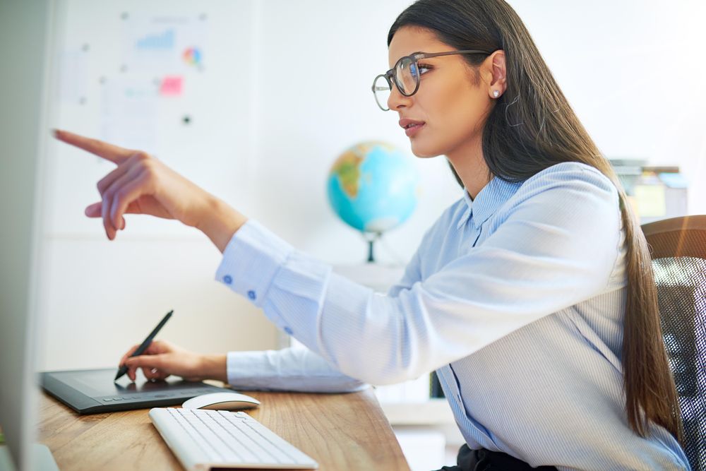 Female graphic designer working from pad and pointing at monitor at home office