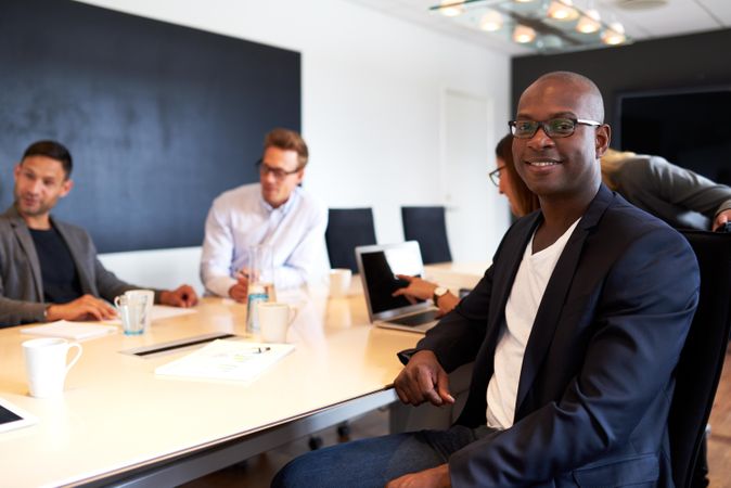 Businessman smiling at camera with colleagues at meeting in background