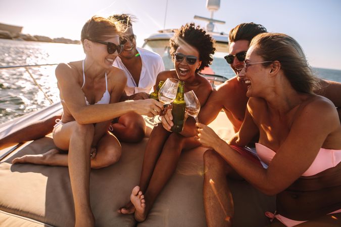 Group of men and women having fun with alcoholic beverages on back of boat