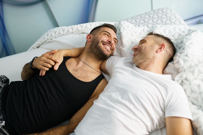 Two men smiling together while lying in bed