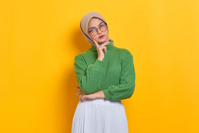 Woman in headscarf and glasses looking up with hand on chin