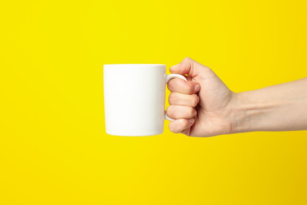 Female hand holding cup on yellow background, space for text