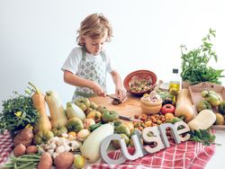 Positive preteen boy cutting vegetables on wooden board while cooking