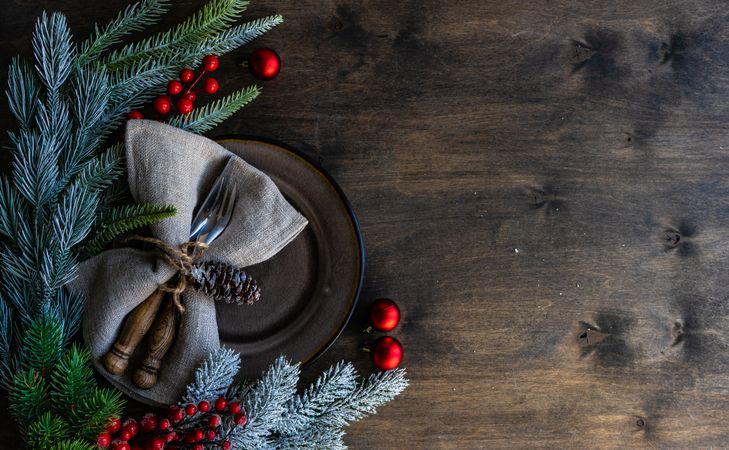 Top view of rustic table setting for Christmas nestled on table with pine and red baubles