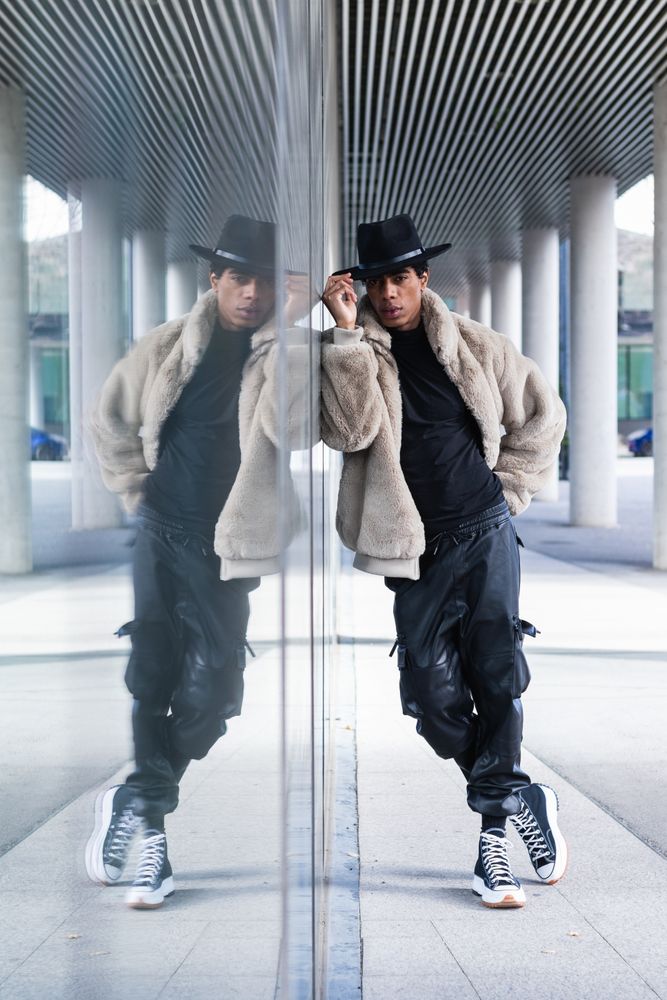 Stylish hispanic man reflecting in glass wall on street