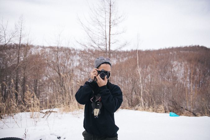 Man in dark sweater holding camera near snow covered ground