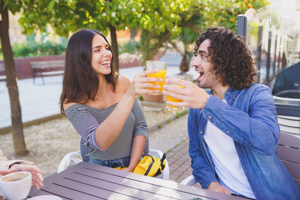 Man and woman toasting with their orange juice outside