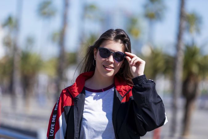 Happy young woman adjusting glasses and looking at camera on sunny day