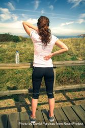 Woman in athletic gear holding hurt upper shoulders overlooking coast, vertical 4AB2qb