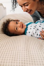 Mother smiling down at happy baby boy on cozy bed