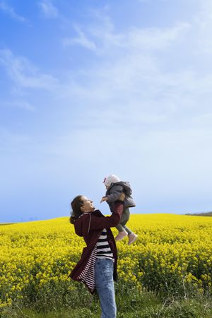 Woman holding up baby in yellow field