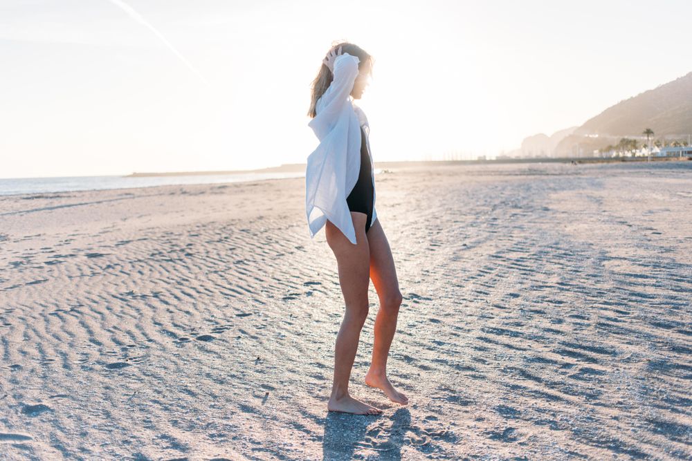 Woman touching hair on beach in oversized shirt