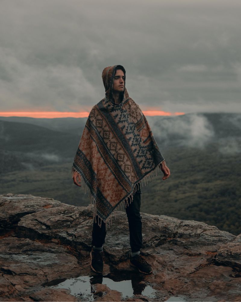 Man in poncho standing on highland at sunset