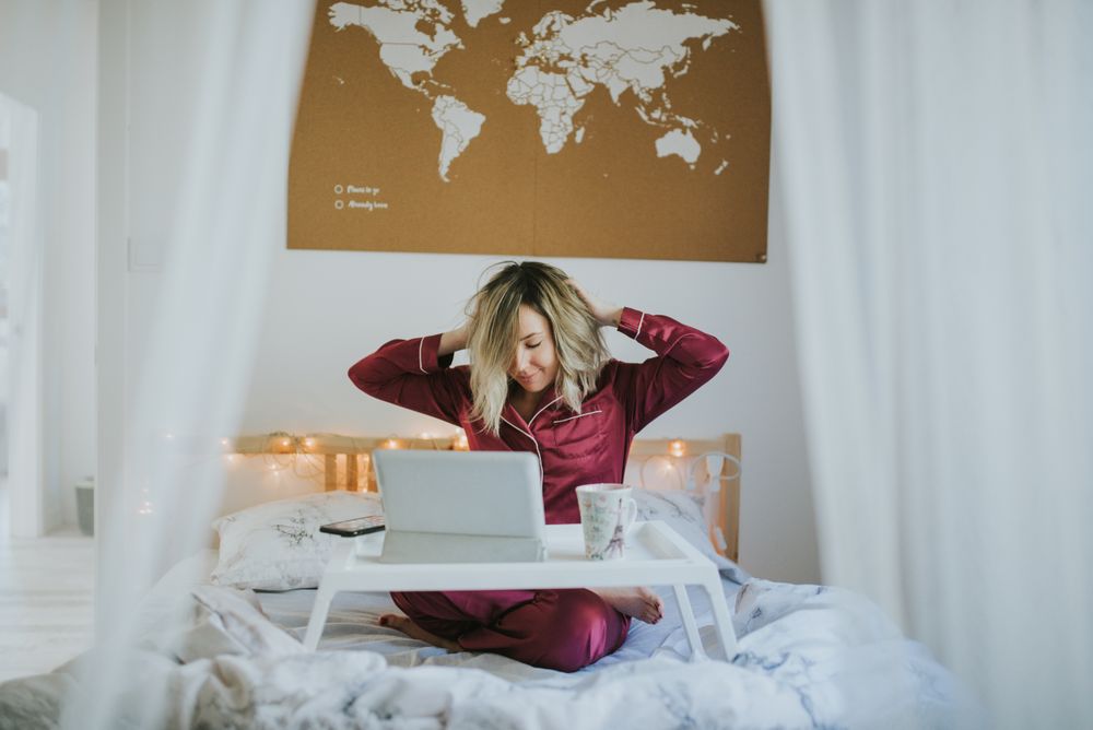 Woman stretching in bed with laptop