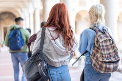 Back of diverse students with books and backpacks walking through campus