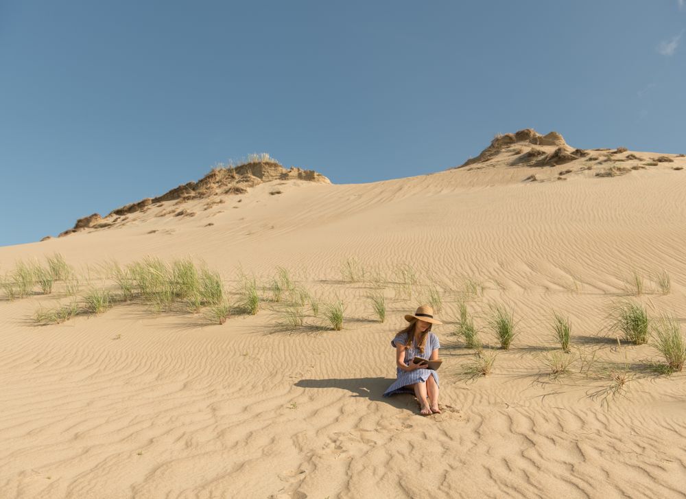 Young woman reading book on sand